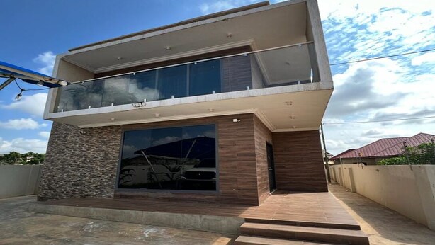 A modern two-story house with a balcony, large windows, and a stone facade.