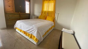 A bedroom with a bed, a window with yellow curtains, a bedside table, and a wooden wall panel. - Increíbles junior suites 1BR (Coconuts 1) (Punta Cana)