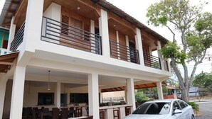 A two-story building with a balcony, a dining area, and a car parked in front. - Increíbles junior suites 1BR (Coconuts 1) (Punta Cana)