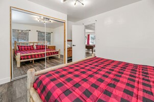 Un dormitorio con un espejo grande, una cama con ropa de cama a cuadros rojos y negros, cabecero de madera y suelo de madera.