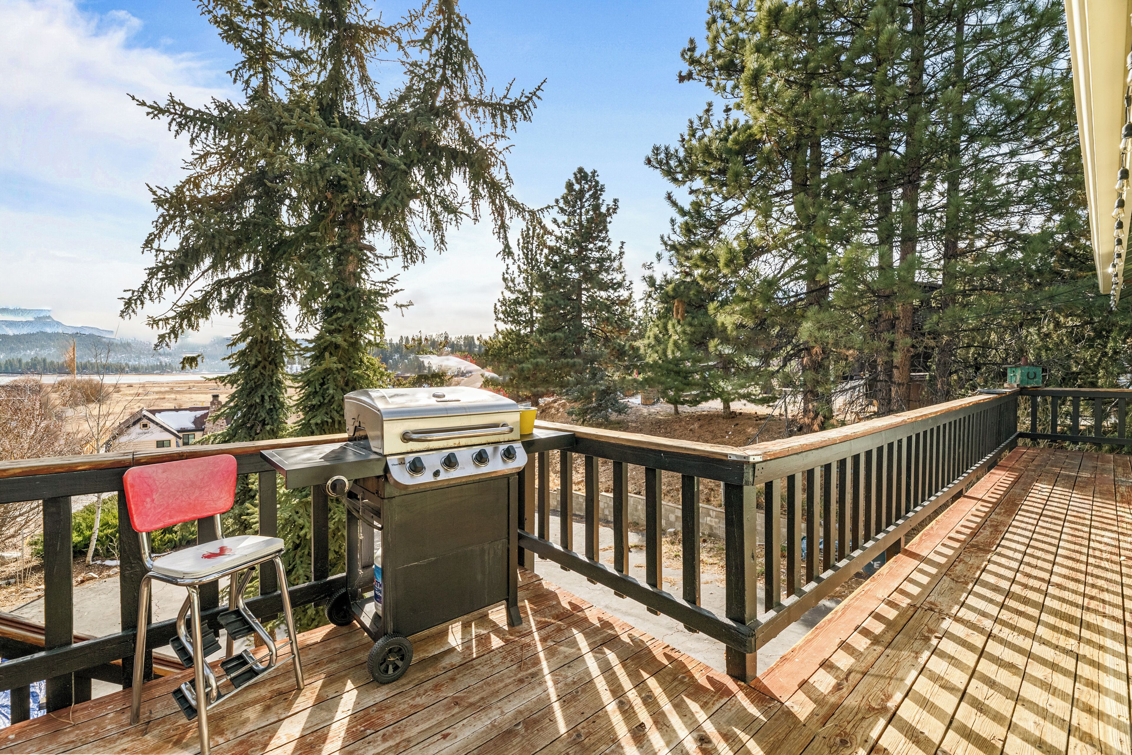 Una terraza de madera con una parrilla y una silla, con vistas a una zona boscosa y montañas al fondo.