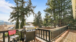 A wooden deck with a grill and a chair, overlooking a forested area with mountains in the background.