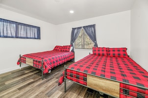 Una habitación con dos camas, cada una con una colcha roja y negra a cuadros, una ventana con cortinas azules y suelo de madera.
