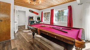 A pool table with a red felt surface, wooden flooring, and a ceiling with wooden beams and lights.