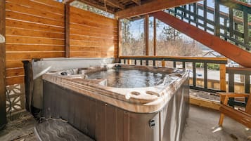 A wooden deck with a hot tub, wooden railings, and a view of the surrounding trees.