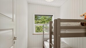 Une chambre avec des lits superposés, aux murs blancs et dotée d’une fenêtre donnant sur un espace verdoyant.