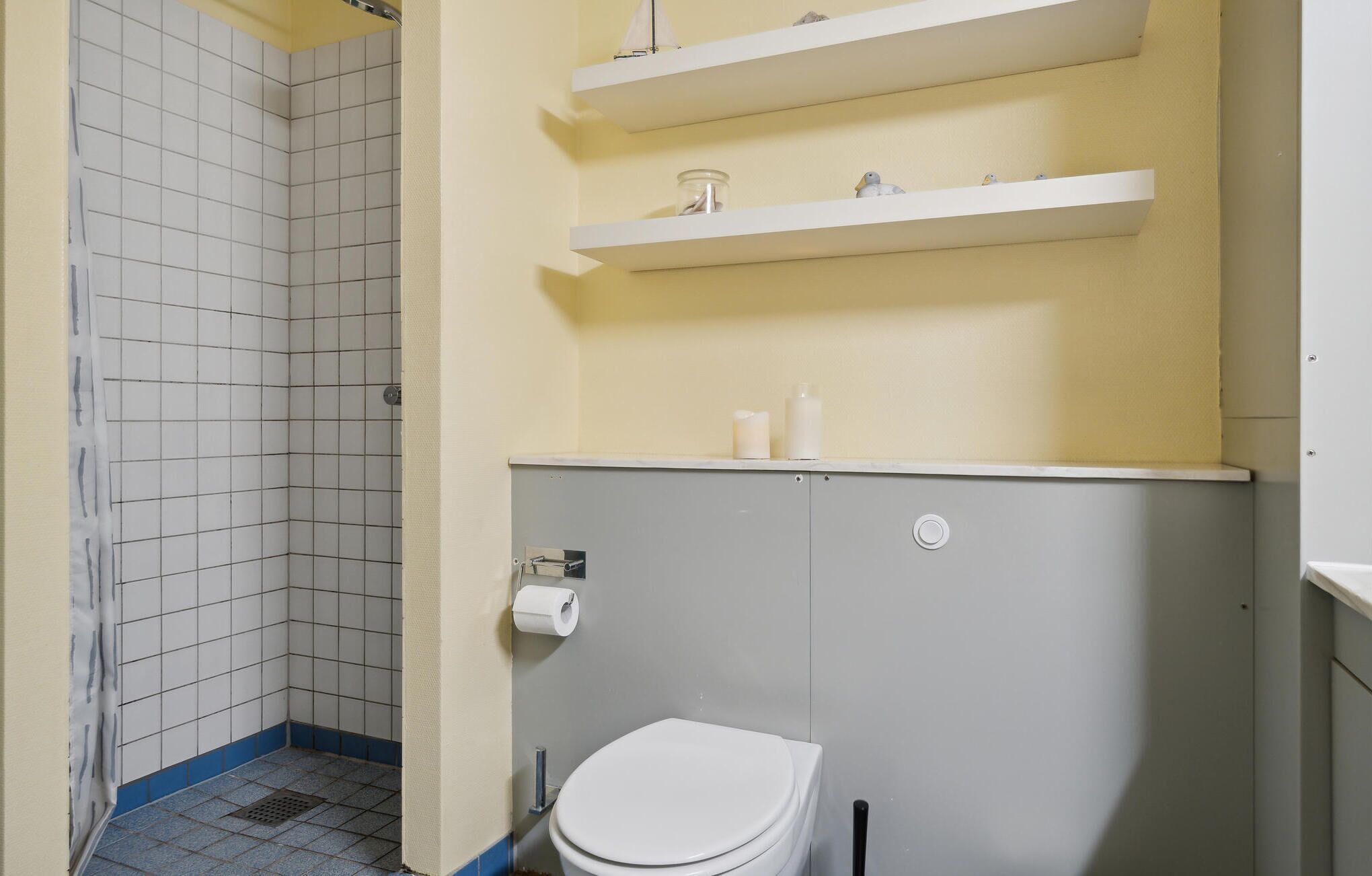 A small bathroom with a toilet, a shower, and a shelf with toiletries.