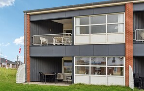 Un immeuble de deux étages doté d’un balcon à l’étage supérieur, avec des rampes en métal et une chaise.