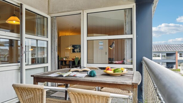 Un balcon avec une table en bois, des chaises en osier et un panier de fruits.