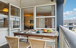 Un balcon avec une table en bois, des chaises en osier et un panier de fruits.