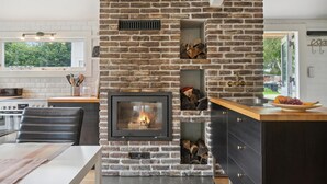A modern kitchen with a built-in fireplace, a dining area, and a view of the outdoors. - Gorgeous home in Jægerspris (Jægerspris)