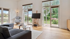 A spacious living room with a grey sofa, a small round table, and a painting on an easel. - Gorgeous home in Jægerspris (Jægerspris)