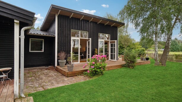 A modern black house with a wooden deck, large windows, and a well-maintained garden with pink flowers. - Gorgeous home in Jægerspris (Jægerspris)