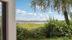 A view of a grassy field with a body of water and distant power lines. - Gorgeous home in Jægerspris (Jægerspris)