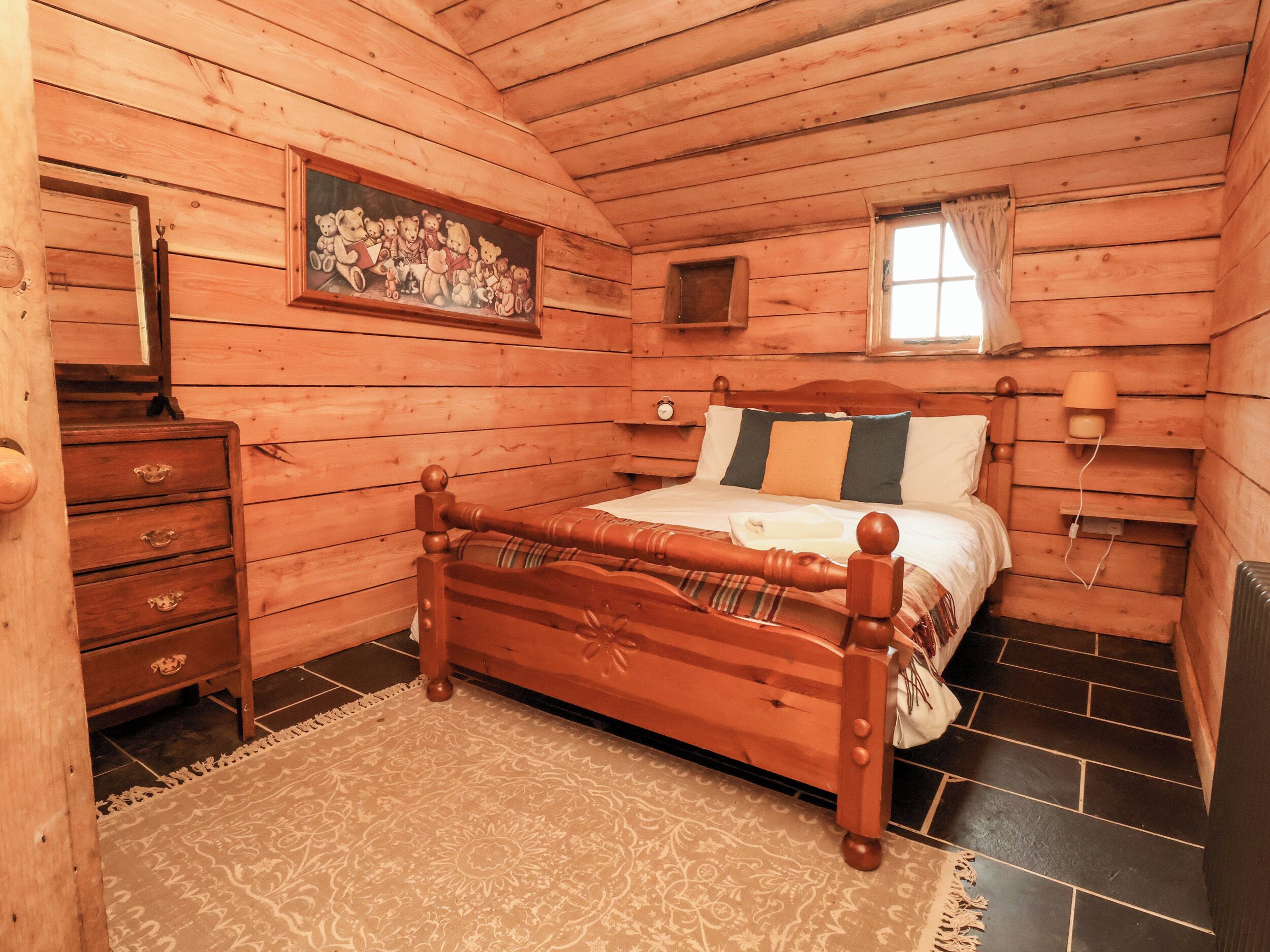 A wooden cabin bedroom with a bed, dresser, and a painting of bears.