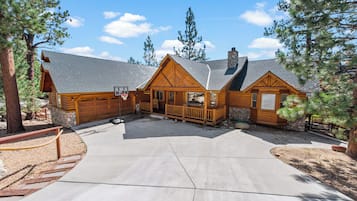 A log cabin with a stone chimney, a basketball hoop, and a porch with a railing.