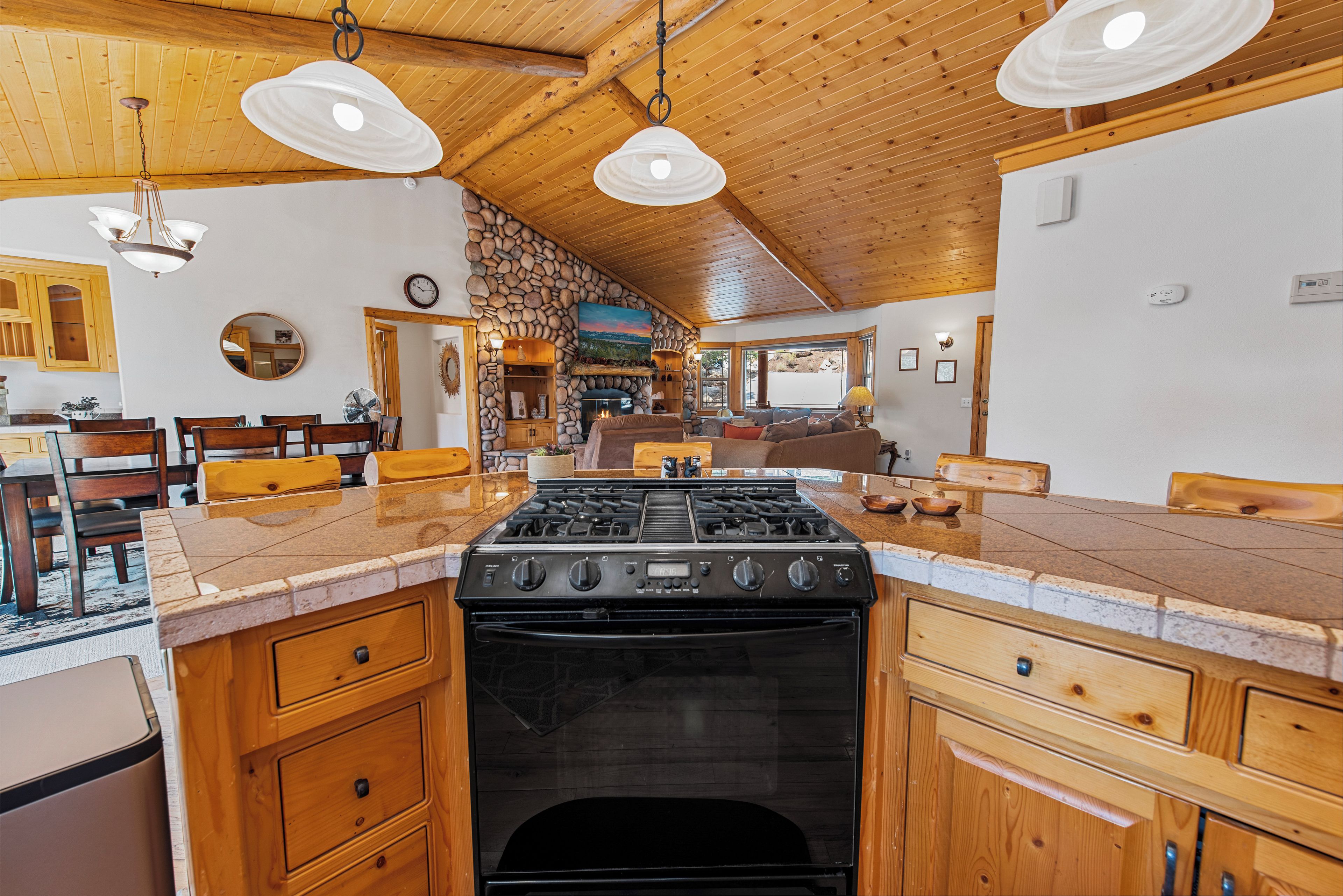 Une cuisine avec un îlot central servant de cuisinière, des armoires en bois et un mur en pierre.