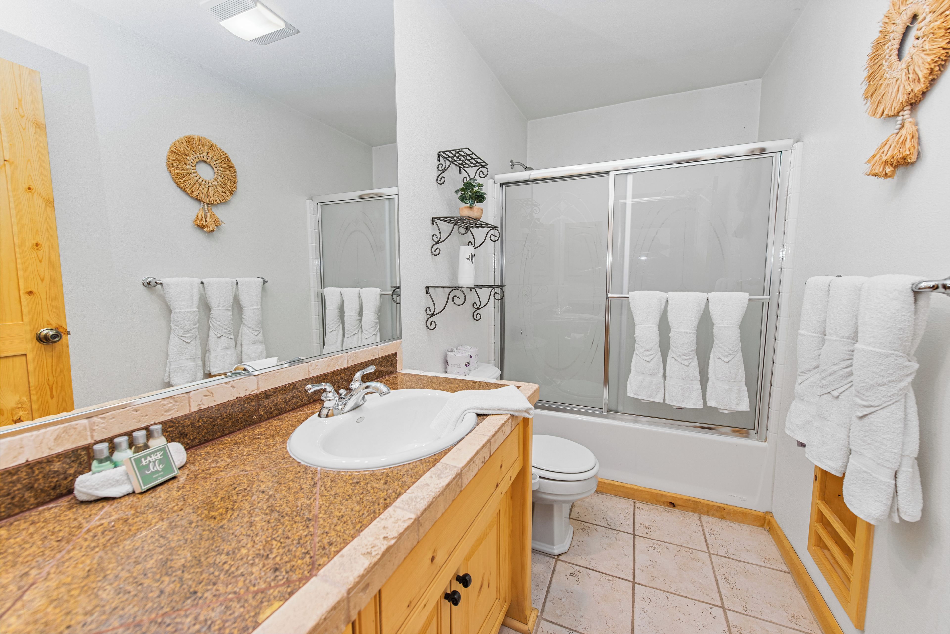 A bathroom with a granite countertop, white sink, wooden vanity, a large mirror, a shower enclosure, and a toilet.