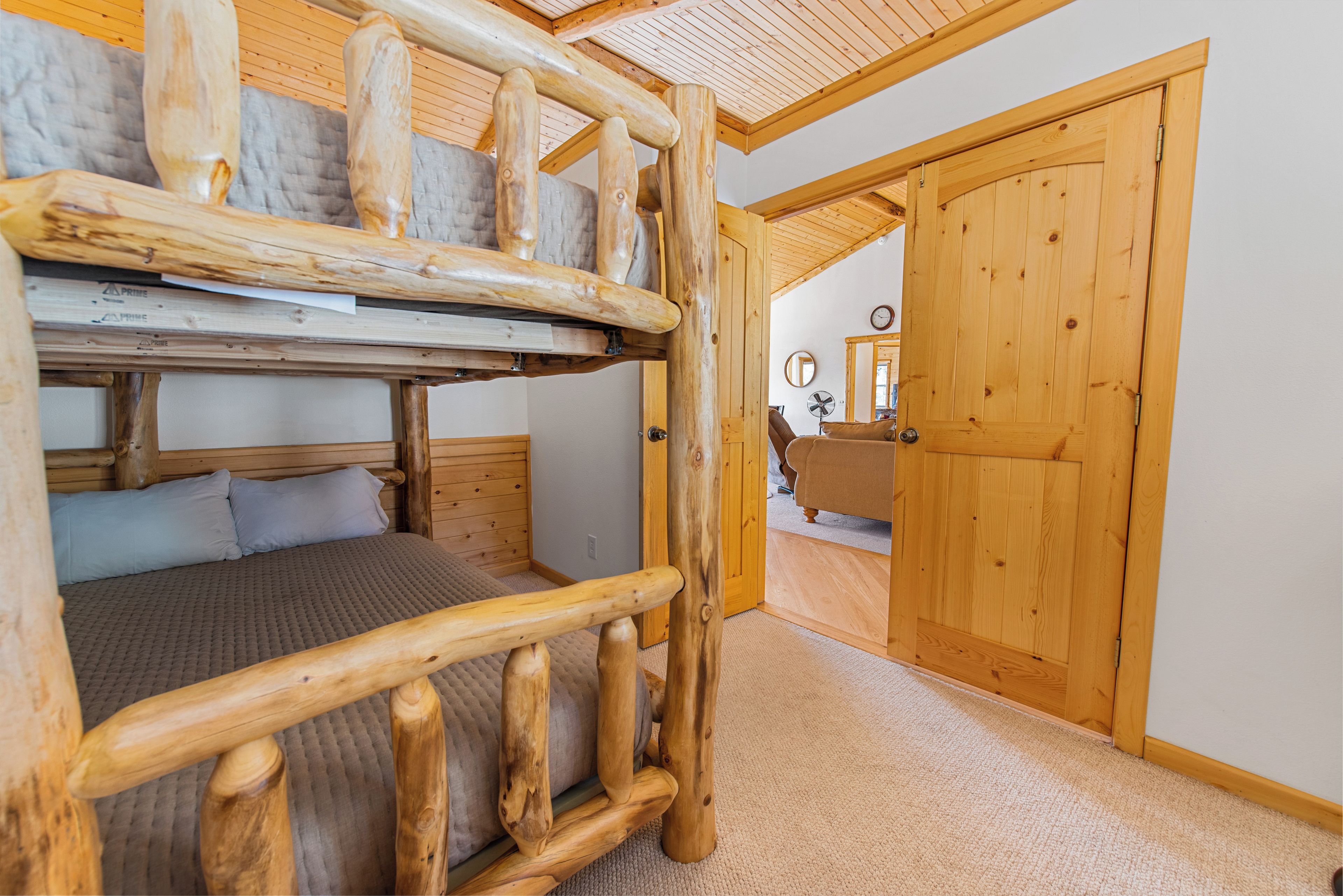 Un lit superposé avec des barreaux en bois, un sol recouvert d’une moquette et une porte en bois à l’arrière-plan.
