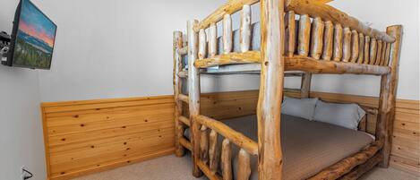 A bunk bed with a wooden frame and a mattress, a wall-mounted television, and a wooden headboard.