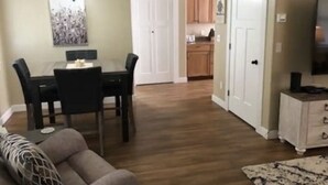 Un comedor con una mesa y sillas, un sofá, un televisor y una cocina al fondo.