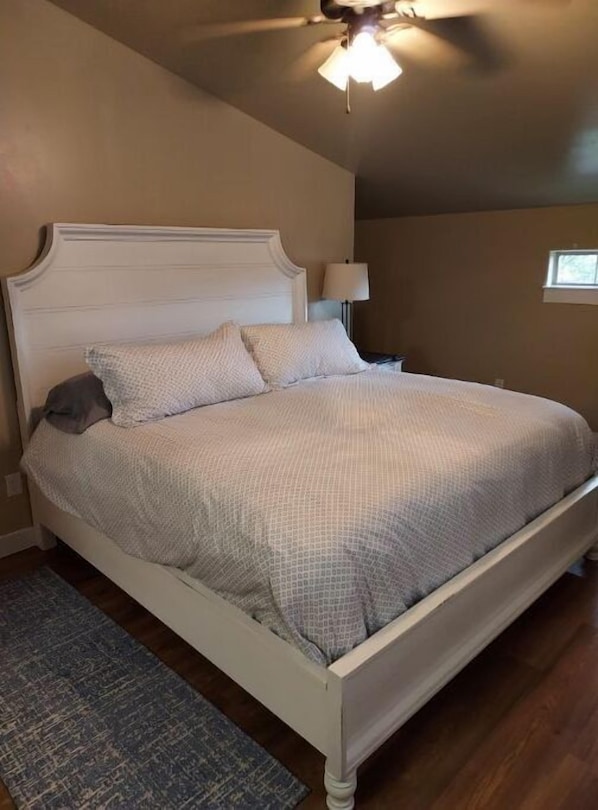 A bedroom with a bed, a ceiling fan, a nightstand, a lamp, and a window.