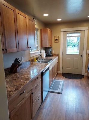 A kitchen with wooden cabinets, a granite countertop, a dishwasher, and a door leading to a garden.