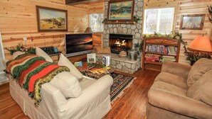 A cozy cabin interior with a stone fireplace, a television, a bookshelf, and a comfortable seating area. - Knotty Knight  (Big Bear Lake)