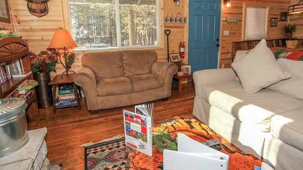 A cozy cabin interior with a sofa, a coffee table, a bookshelf, and a dining table. - Knotty Knight  (Big Bear Lake)