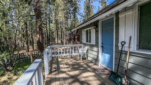 A wooden deck with a white railing, a blue door, and two shovels leaning against the house. - Knotty Knight  (Big Bear Lake)