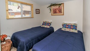 A room with two beds, a window with blinds, a framed picture, and a small plant. - Knotty Knight  (Big Bear Lake)