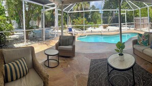 Eine überdachte Terrasse mit Pool, Korbmöbeln und Blick auf den Garten.