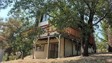 A two-story house with a wooden deck and a staircase leading to the upper level.