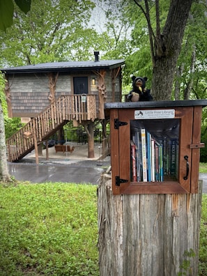 En träkonstruktion med en trappa, en björnstaty och en bokhylla med texten ”Litet bibliotek – böcker för alla” i en park.