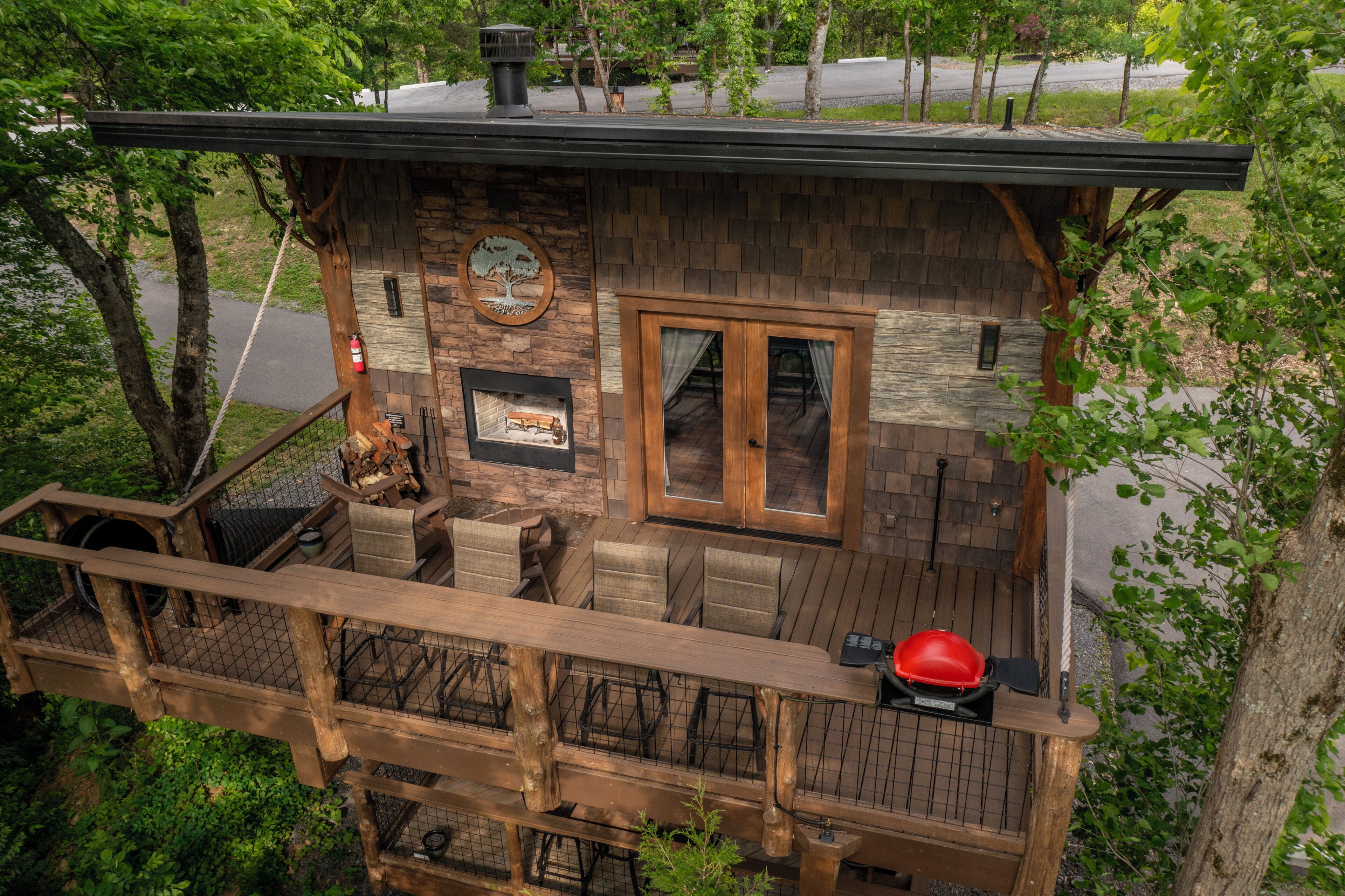 Une terrasse en bois avec des meubles d’extérieur, une cheminée en pierre et une vue sur la verdure environnante.