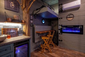 A kitchen with a built-in oven, a wooden table, and a wall-mounted fish tank. - Smoky Mountain Treehouse | 20-ft Slide + Hidden Crank-Out Bed | Sleeps 6 (Sevierville)