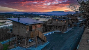 A series of wooden cabins with external staircases, connected by a paved walkway, set against a mountainous backdrop. - Family Treehouse beside the Firepit | 20-Ft Slide, Swings + Drink Chute (Sevierville)