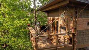 Une cabane dans les arbres dotée d’une terrasse en bois, d’une échelle de corde et d’un petit espace clos contenant un extincteur.