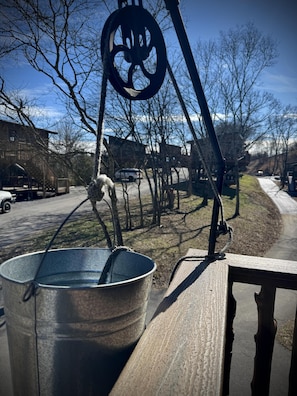 A metal bucket on a wooden surface with a pulley system above it, set against a backdrop of leafless trees and a clear sky. - Family Adventure Treehouse | 20-ft Slide + Secret Beds | Sleeps 6 | Smoky Mtns (Sevierville)
