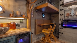 A kitchen with wooden cabinets, a dish rack, and a wooden chair. - Family Adventure Treehouse | 20-ft Slide + Secret Beds | Sleeps 6 | Smoky Mtns (Sevierville)
