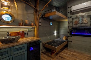 Habitación pequeña con cama, un lavamanos, estante de madera y aire acondicionado de pared.