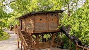 A wooden cabin with a staircase, a slide, and a deck. - Family Adventure Treehouse | 20-ft Slide + Secret Beds | Sleeps 6 | Smoky Mtns (Sevierville)