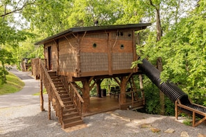 Une cabane en bois avec un escalier, un toboggan et une terrasse.