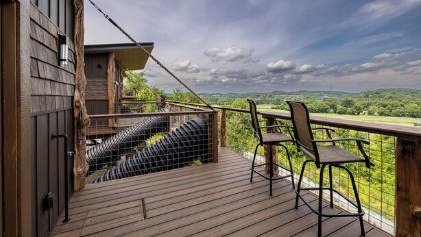 Una terraza de madera con vistas a colinas verdes, una silla y una barandilla.