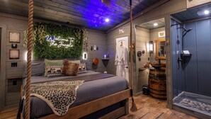 Una habitación con cama, techo de madera, pared con el letrero 'Welcome to the Jungle', un espejo y zona de ducha.
