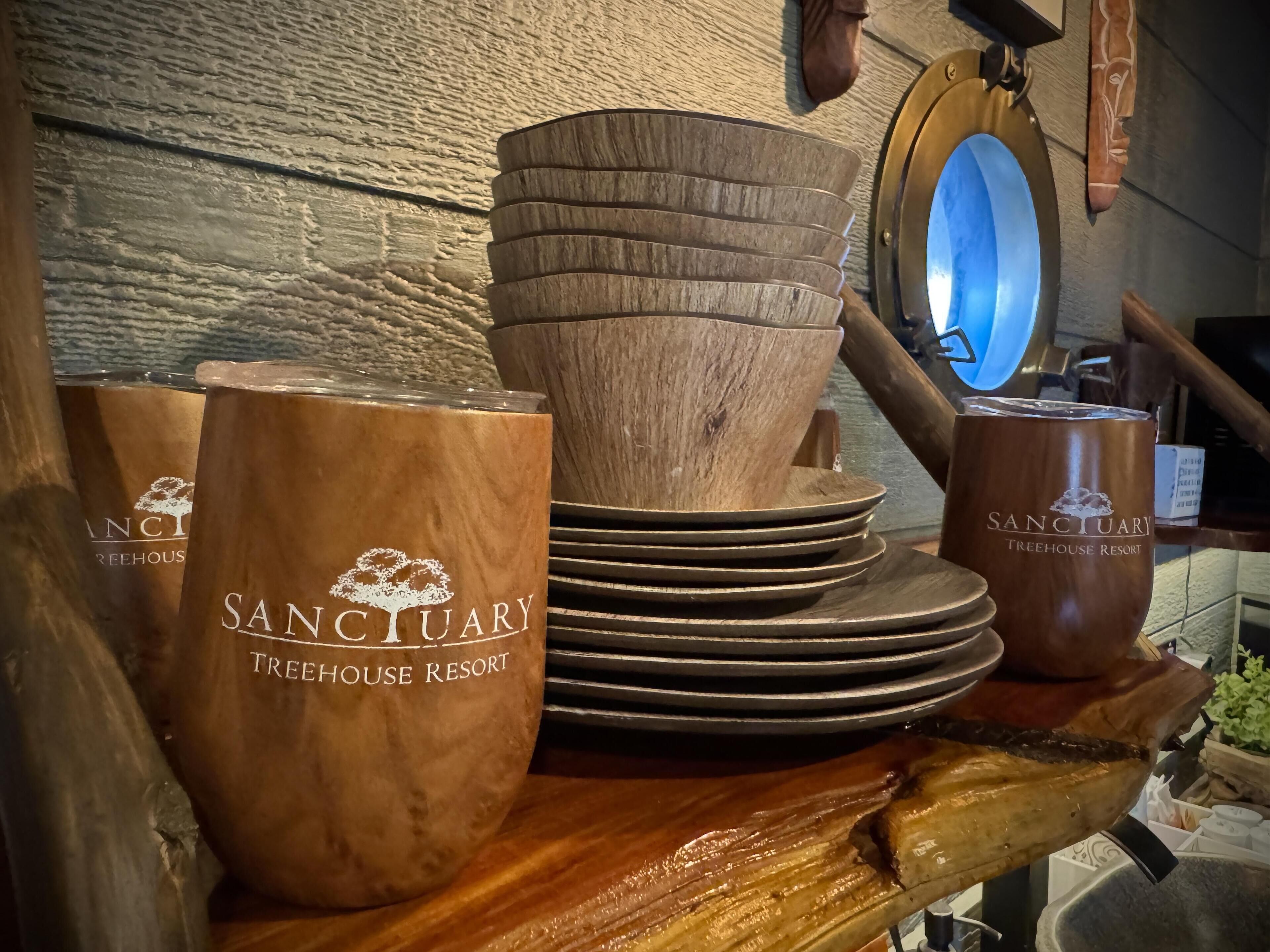 Une pile de bols et de tasses en bois, portant l’inscription « Sanctuary Treehouse Resort », est posée sur une surface en bois.