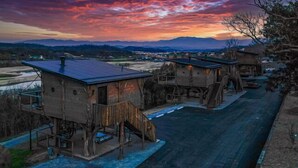 Une rangée de cabanes rustiques en bois, dotées d’escaliers extérieurs, se dressant sur fond de coucher de soleil sur un paysage montagneux.