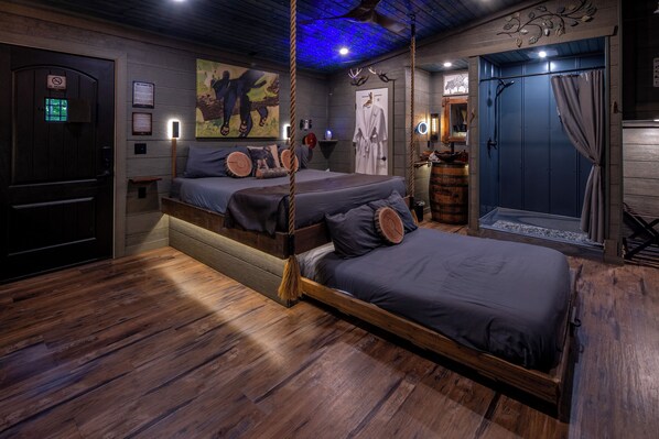 Una habitación con dos camas, piso de madera, puerta azul y un columpio de cuerda colgando.