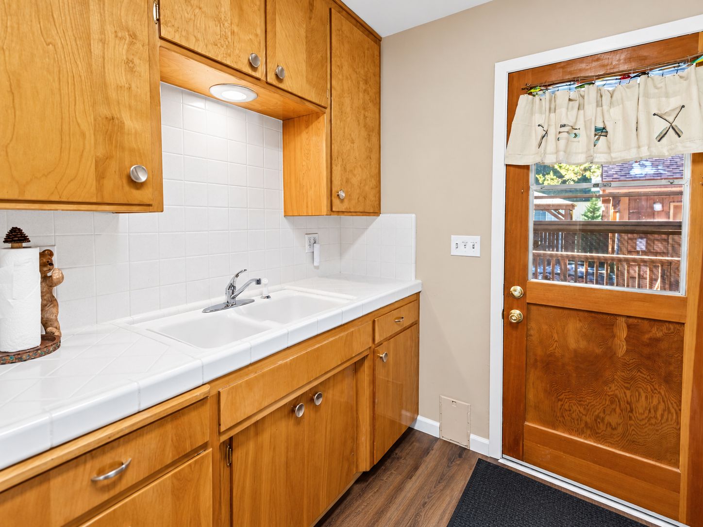 A kitchen with wooden cabinets, a white countertop, a sink, and a door with a window.