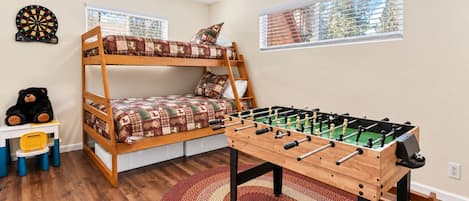 A bunk bed with a dartboard and a foosball table in a room with wooden flooring and a red patterned rug.